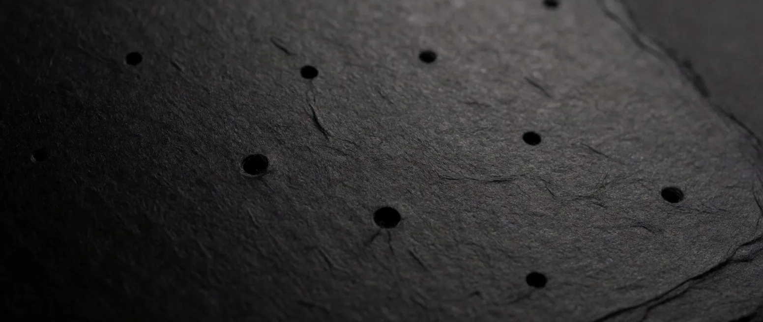 Close-up of perforated gummed paper texture with amber raked light